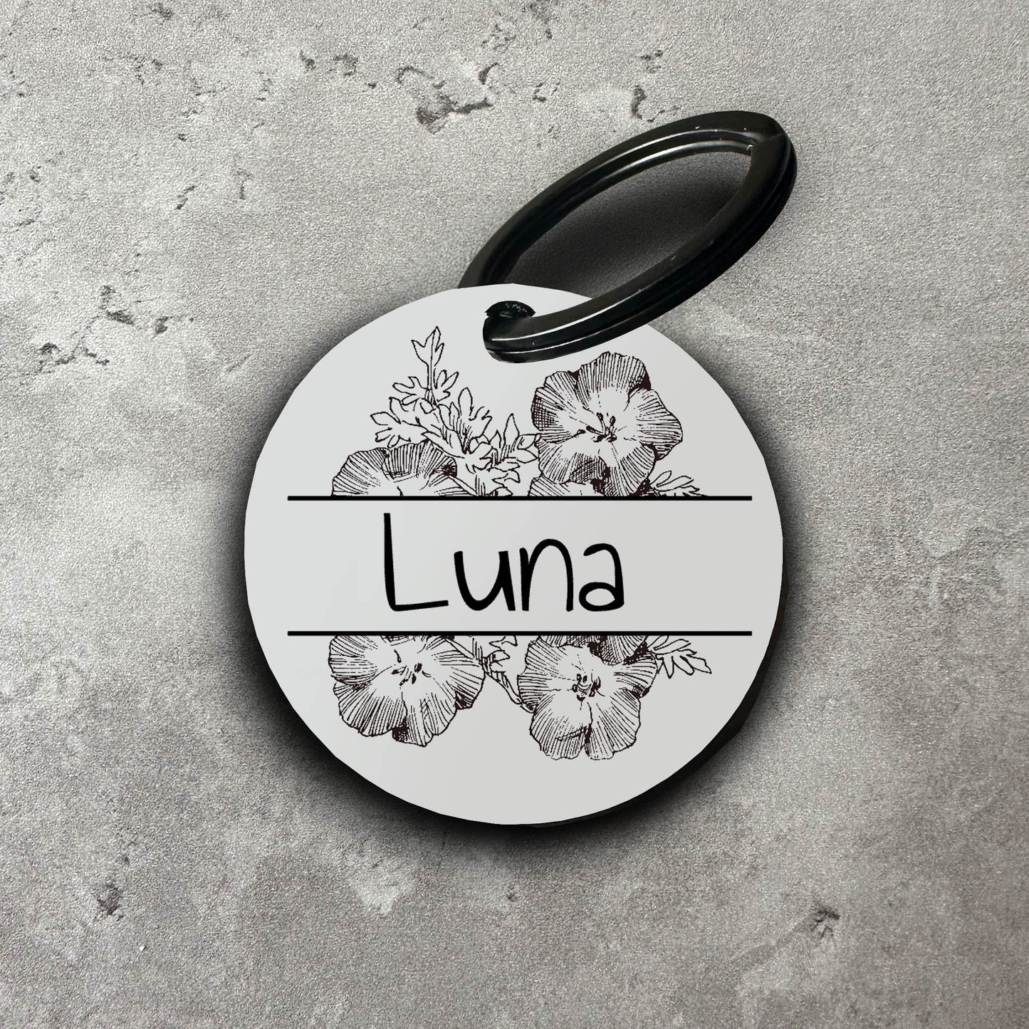 Vit rund namnbricka för hund med dekorativa blommor som mönster och namnet Luna, monterad på svart nyckelring